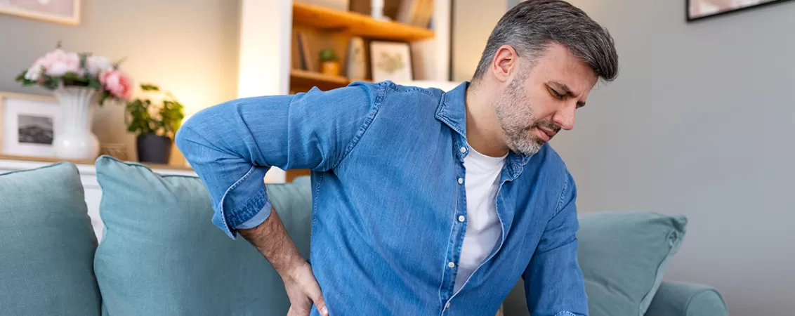Barbat cu dureri de spate stand pe o canapea.