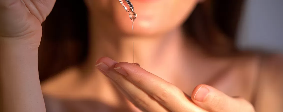 Mainile unei femei care isi aplica ulei de batana in palma cu o pipeta