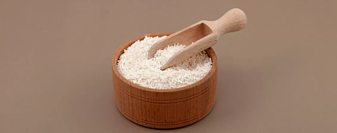 Granule de sorbat de potasiu pe o lingura de lemn, ilustrand utilizarea conservantului alimentar in preventia dezvoltarii microorganismelor.