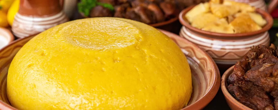 Mamaliga rasturnata pe o farfurie, langa farfurii cu carne si branza