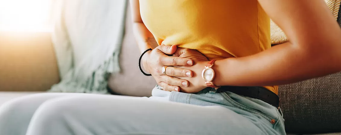 Femeie care sta pe canapea, cu mainile pe abdomen, suferind de dureri menstruale