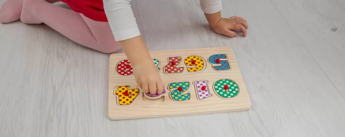 Fetita mica se joaca cu un puzzle din lemn pentru dezvoltare cognitiva
