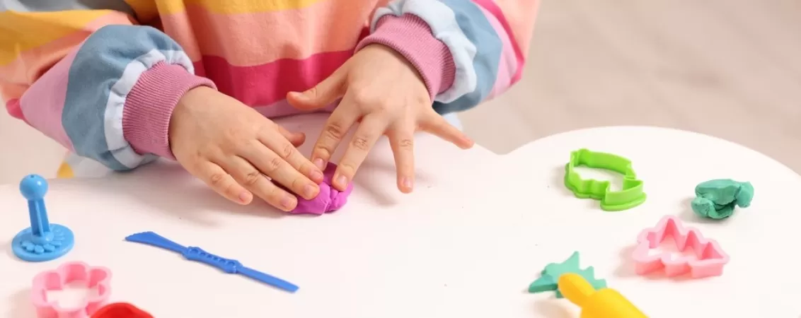 Mainile unei fetite ce se joaca cu plastilina