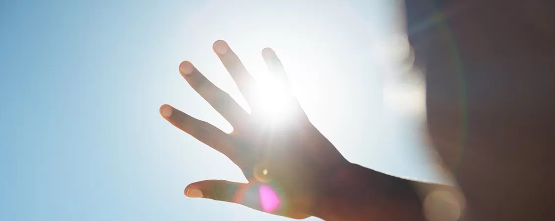 Persoana incercand sa blocheze lumina soarelui cu mana.