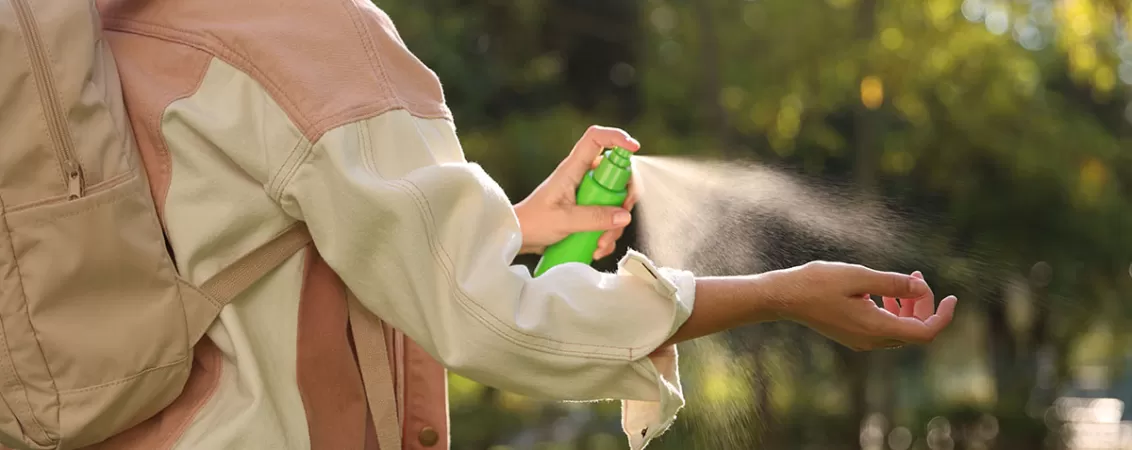 Femeie aplicand spray anti-capuse pe mana in timpul unei drumetii.