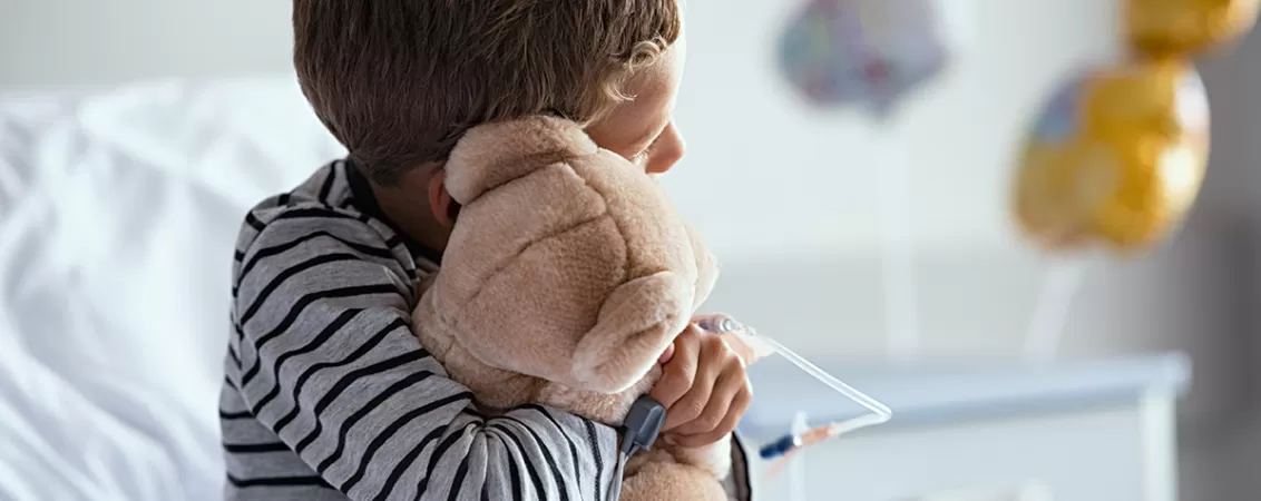 Copil internat la spital cu branulă care ține ursuleț de pluș în brațe