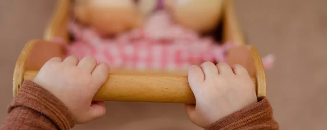 Copil mic jucandu-se cu un carucior si papusa intr-o sala de clasa Waldorf.