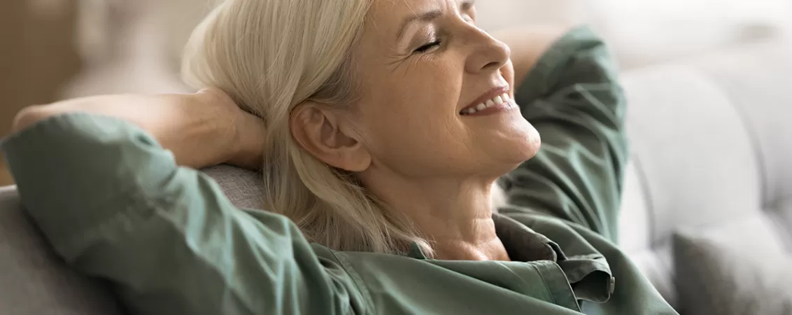 Femeie la menopauza stand relaxata o canapea, cu mainile sub cap si cu ochii inchisi.