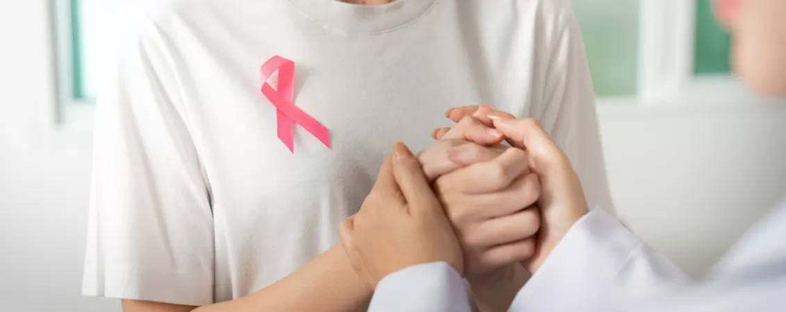Doua femei se tin de mana oferind sprijin in lupta impotriva cancerului mamar