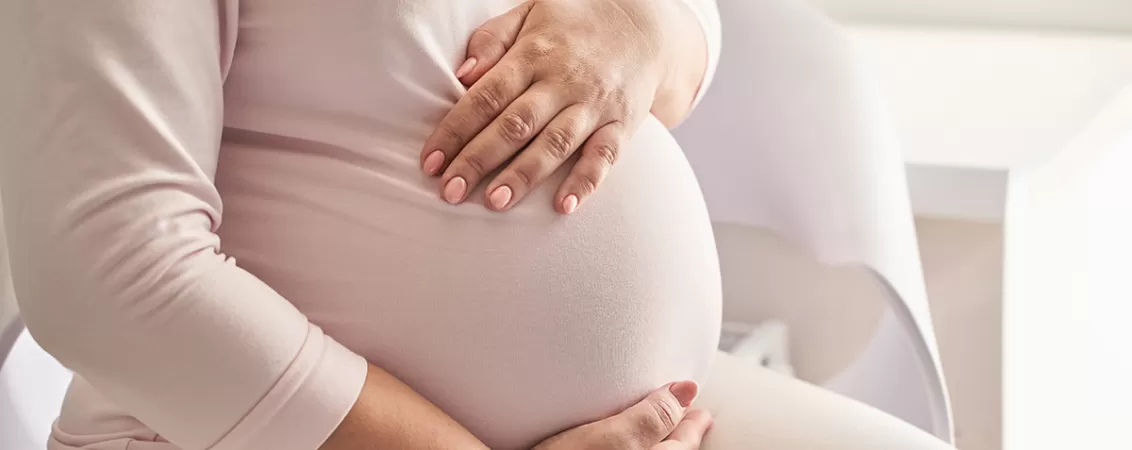 Femeie insarcinata sta pe canapea si isi atinge burtica