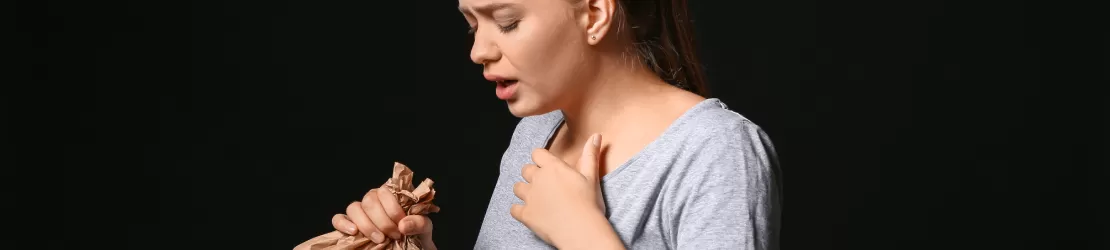 Femeie care sufera de hiperventilatie si tine in mana o punga de hartie