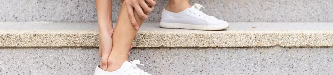 Femeie care sta pe niste scari si isi maseaza glezna