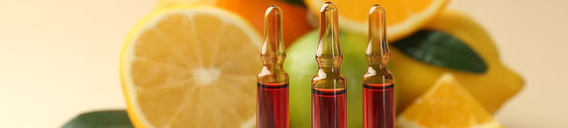 Fiole cu vitamina C pentru ingrijirea pielii, alaturi de diverse citrice proaspete