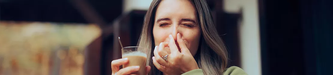 Femeie care isi acopera nasul, deranjata de mirosul unei bauturi cu cofeina, indicand o reactie olfactiva puternica