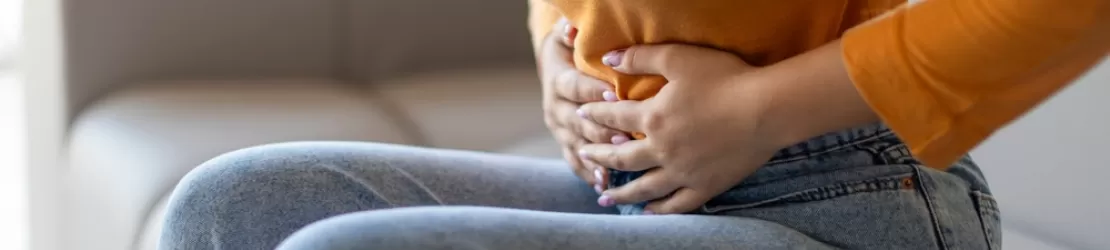Femeie care sufera de dureri abdominale, stand pe canapea cu mainile pe abdomen