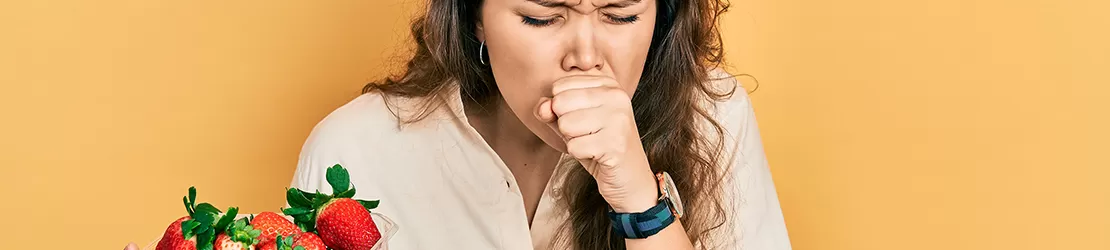 Femeie care tine o caserola de capsuni in mana si tuseste ca simptom al alergiei la capsuni
