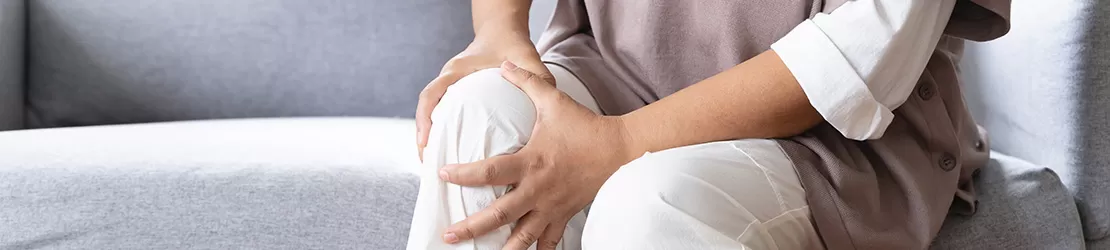 Femeie in varsta cu durere la nivelul genunchiului, simbolizand artrita reumatoida sau afectiuni articulare cronice