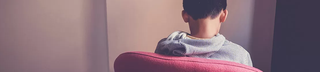 Baiat preadolescent trist asezat singur pe un fotoliu, fotografiat din spate