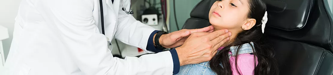 Medicul examineaza gatul unei fetite bolnave in cabinetul medical.