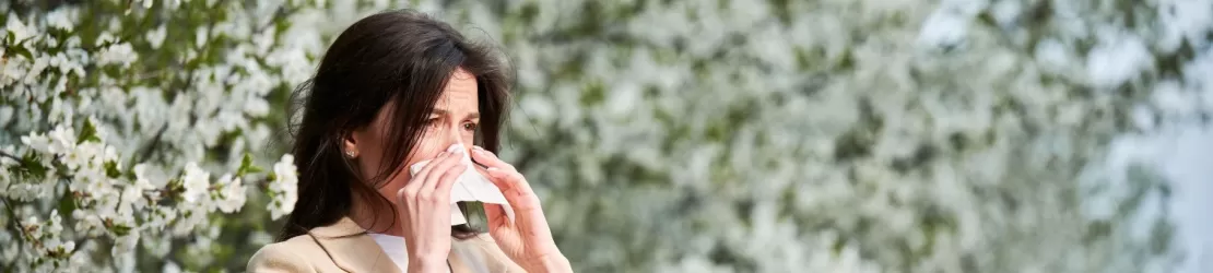 Femeie care sufera de alergii sezoniere care se manifesta prin secretii nazale, stergandu-se cu un servetel