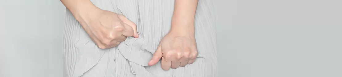 Partea inferioara a unei femei care prezinta simptome de leucoree si isi tine strans fusta in incercarea de a controla aceste simptome