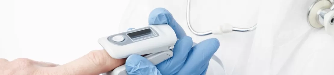 Prim-plan cu un medic care foloseste un pulsoximetru pe degetul pacientului pentru masurarea oxigenului din sange