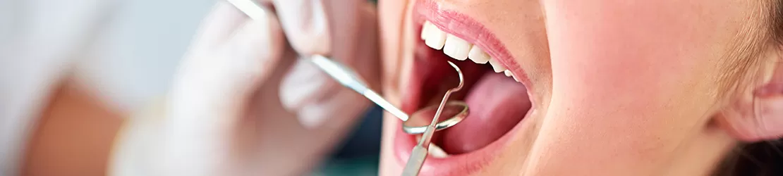 Fetita la dentist, cu gura deschisa in timpul inspectiei orale, medicul verificand sanatatea dintilor si a gingiilor