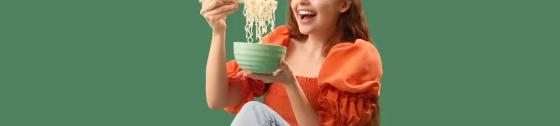 femeie tanara fericita in timp ce mananca noodles dintr-un bol, ilustrand o masa rapida si obiceiuri alimentare din viata de zi cu zi.