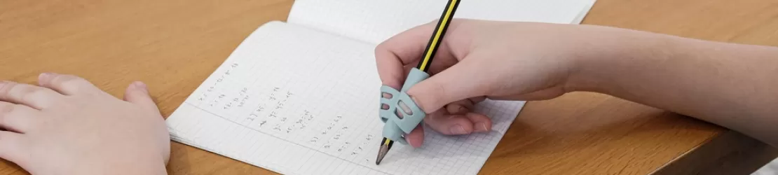 Mana unui copil scrie atent in timp ce realizeaza exercitii la birou