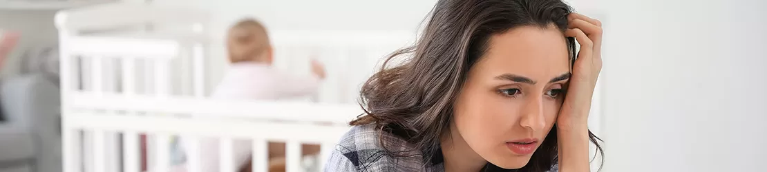 Mama asezata pe jos langa patul in care este un bebelus