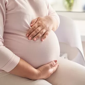 Femeie insarcinata sta pe canapea si isi atinge burtica